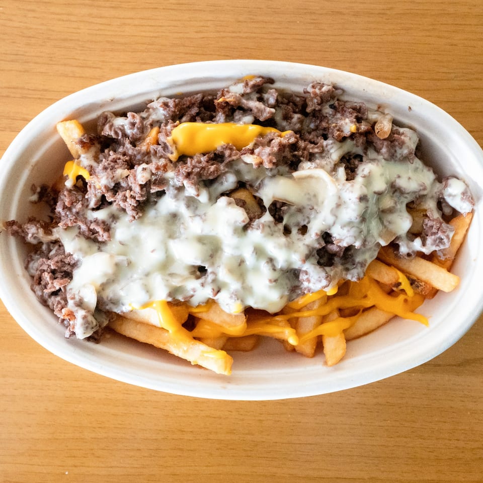 Cheesesteak Grill's fries loaded with melted cheese, steak, and white sauce in a white bowl.