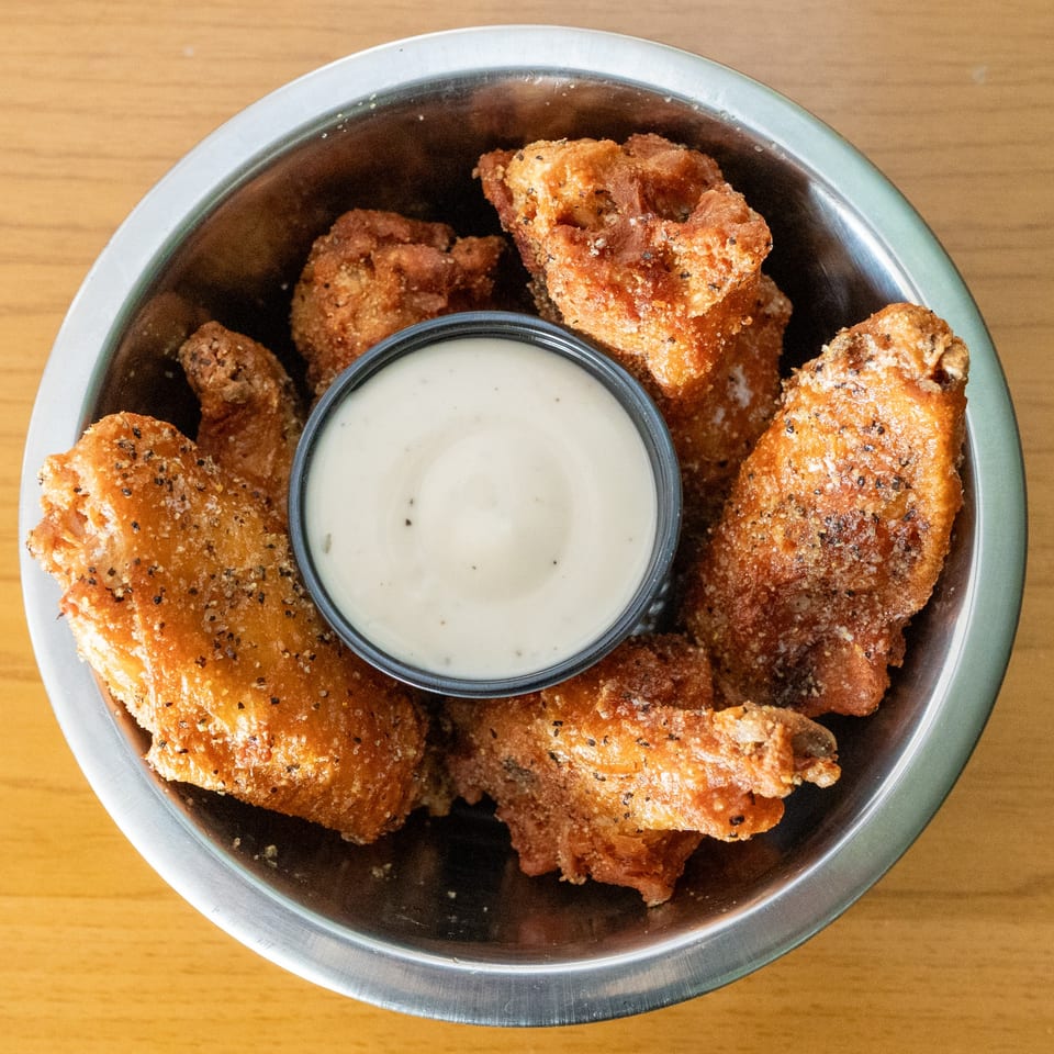 Crispy fried chicken wings with black pepper and salt, served in a metal bowl with ranch dip.